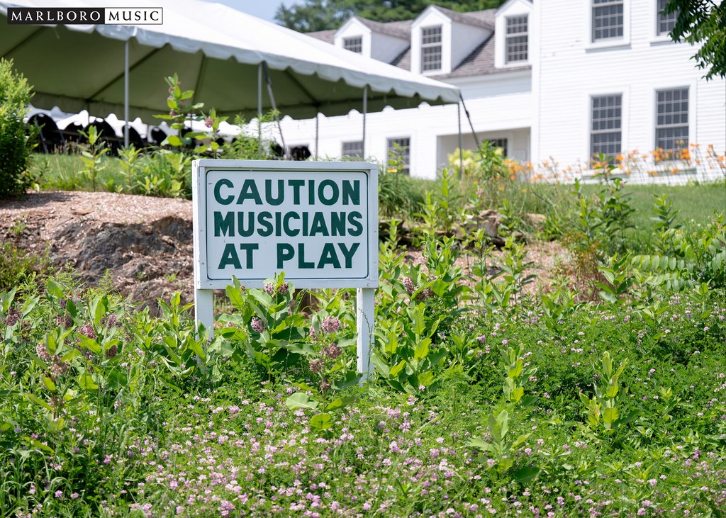 Sign that reads "Caution Musicians at Play" in a grassy field at the Marlboro School of Music