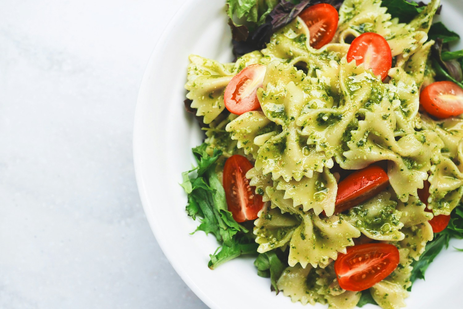 overhead shot of bowtie pasta with greens and tomatoes on a white plate