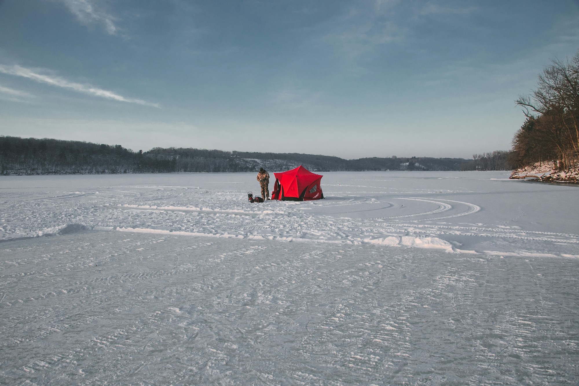 man ice fishing with red tent